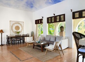A spacious living room with a dining area, large windows with shutters, and a ceiling mural.