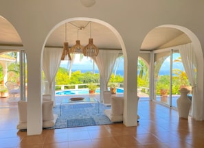 A spacious room with a pool, white arches, and a view of the ocean.