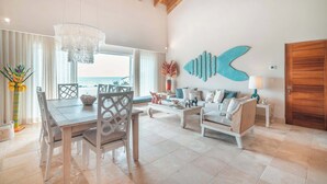 A spacious living area with a dining table, chairs, a sofa, and a large fish wall art piece. - Beachfront Apartment with Private Jacuzzi cap cana (Punta Cana)