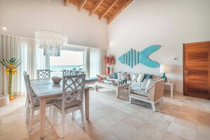 A spacious living area with a dining table, chairs, a sofa, and a large fish wall art piece. - Beachfront Apartment with Private Jacuzzi cap cana (Punta Cana)