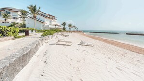 A beach with a concrete walkway, palm trees, and a building with multiple balconies. - Beachfront Apartment with Private Jacuzzi cap cana (Punta Cana)