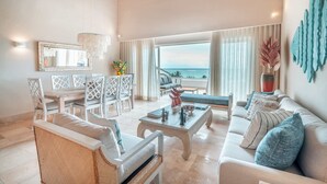 A spacious living room with a view of the sea, a dining area with white furniture, and a large mirror on the wall. - Beachfront Apartment with Private Jacuzzi cap cana (Punta Cana)
