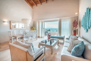 A spacious living room with a view of the sea, a dining area with white furniture, and a large mirror on the wall. - Beachfront Apartment with Private Jacuzzi cap cana (Punta Cana)