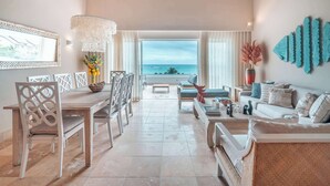 A spacious living room with a view of the ocean, a dining area with a wooden table and chairs, and a cozy seating area with a sofa and a coffee table. - Beachfront Apartment with Private Jacuzzi cap cana (Punta Cana)
