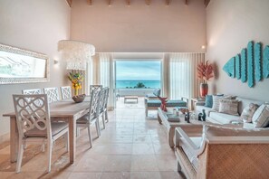 A spacious living room with a view of the ocean, a dining area with a wooden table and chairs, and a cozy seating area with a sofa and a coffee table. - Beachfront Apartment with Private Jacuzzi cap cana (Punta Cana)