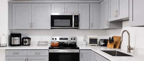 Una cocina moderna con gabinetes grises, un microondas de acero inoxidable, un horno integrado y un lavamanos con un grifo moderno.