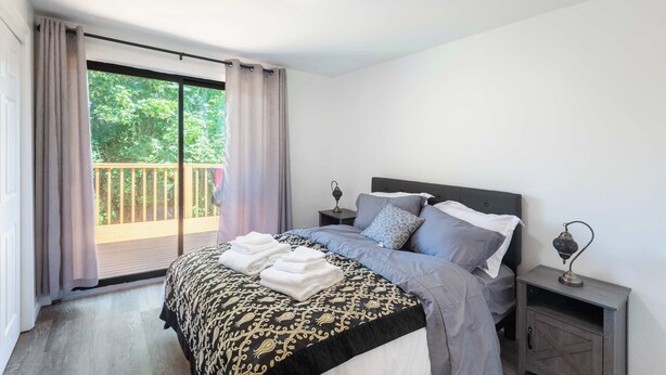 A bedroom with a bed, a nightstand, a lamp, and a balcony with curtains. - Seattle Hillside Escape with Decks & Scenic Views (Seattle)