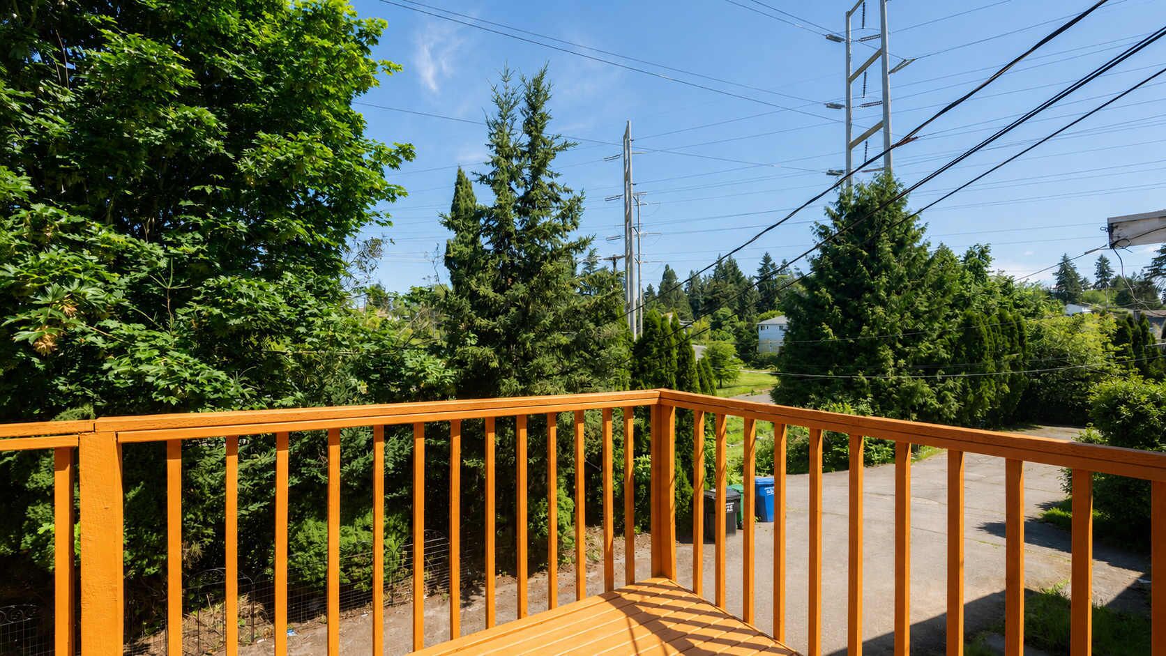 A wooden deck with a metal railing, surrounded by trees and a clear sky.