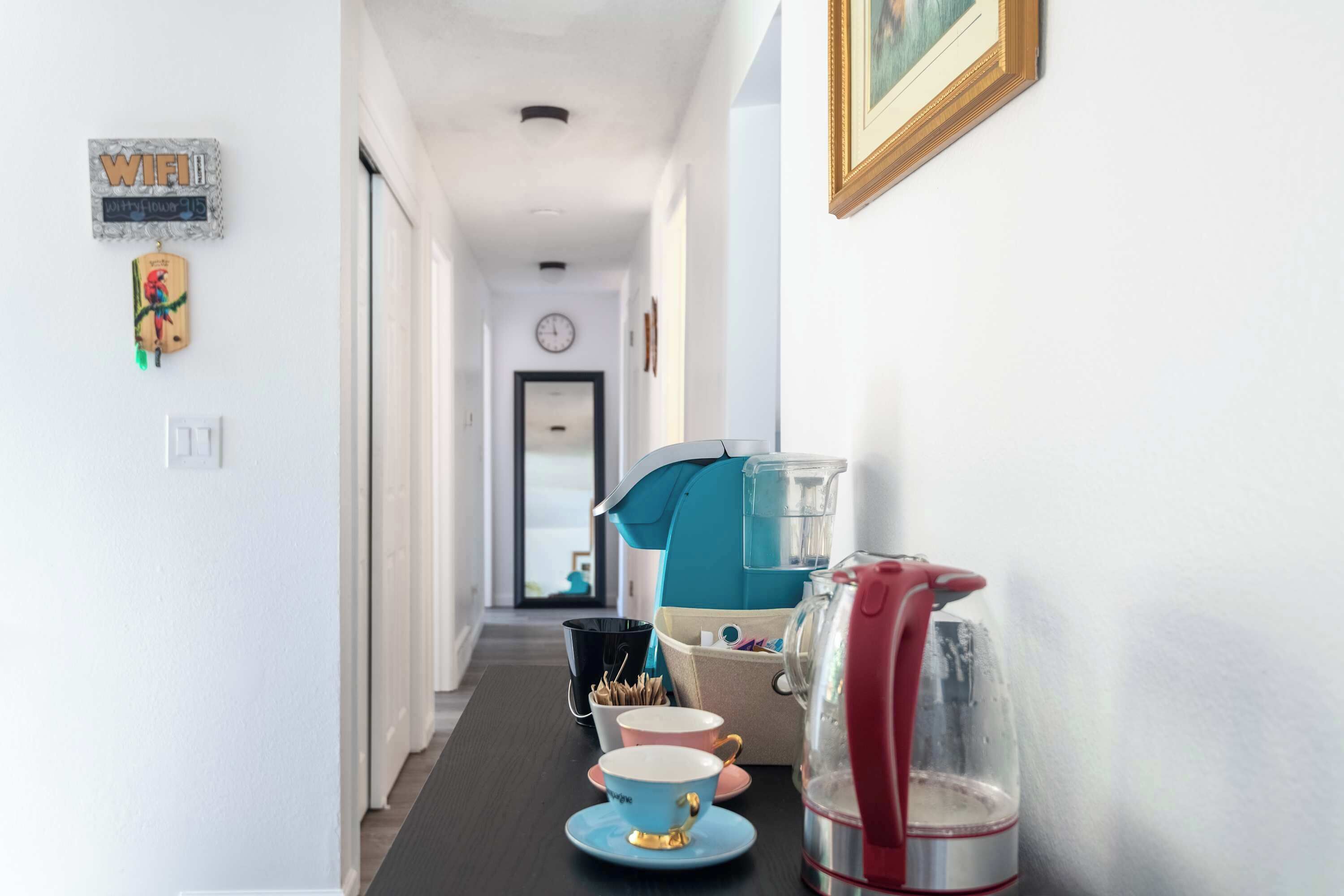 Un couloir avec une machine à café, des tasses et une théière sur une table.