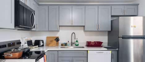 Una cocina moderna con gabinetes grises, un refrigerador de acero inoxidable, un microondas, un lavavajillas y un ventilador de techo.