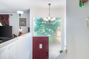A staircase with a red door, a chandelier, a framed picture, and a television. - Seattle Hillside Escape with Decks & Scenic Views (Seattle)