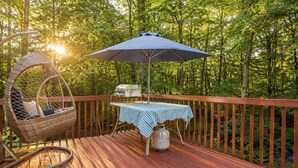 Een houten terras met een rieten stoel, een tafel met een geruit tafelkleed en een barbecue.
