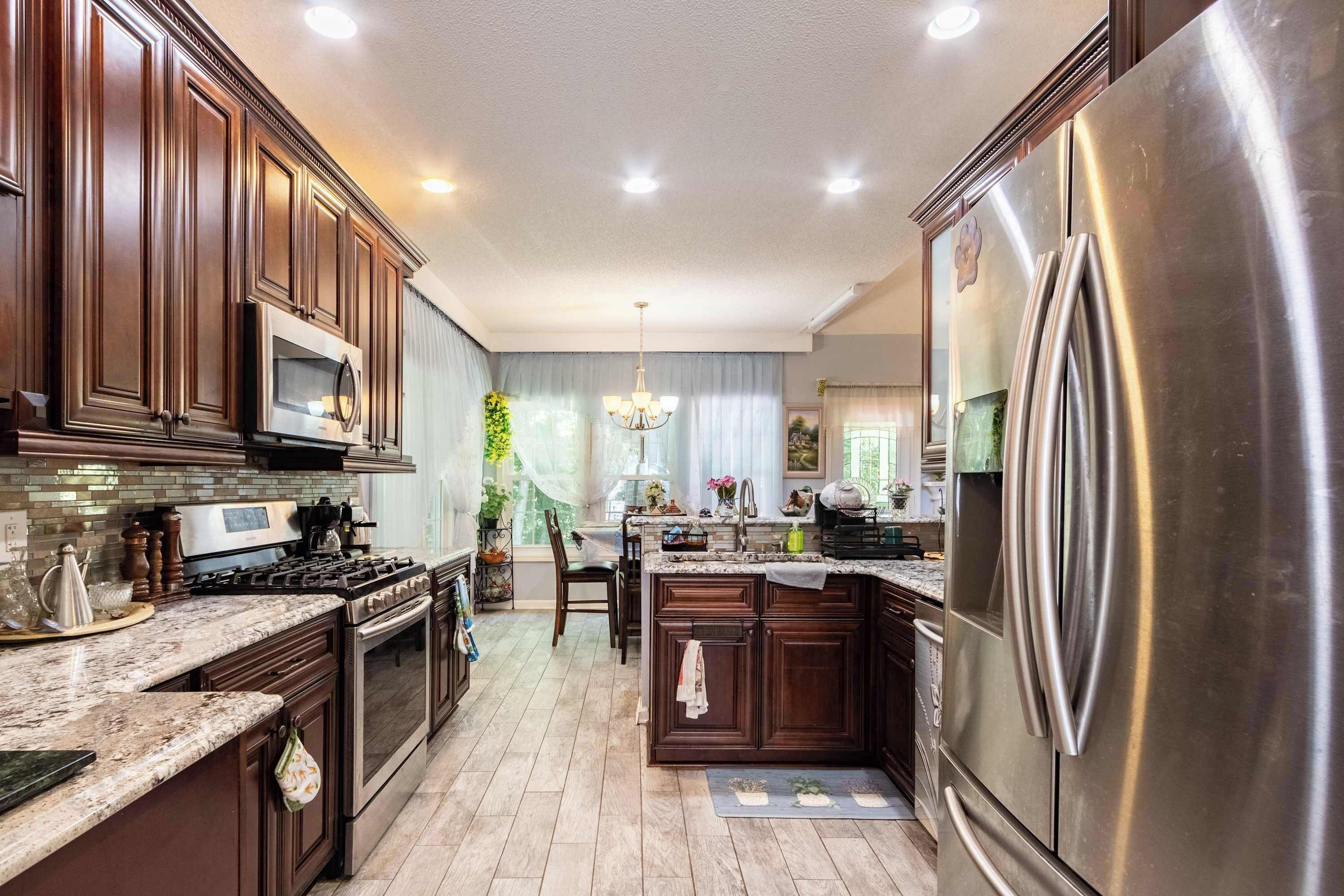 A kitchen with dark wooden cabinets, stainless steel appliances, and a marble countertop.