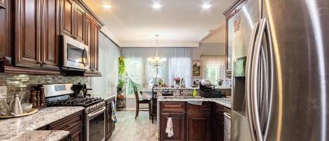 A kitchen with dark wooden cabinets, stainless steel appliances, and a marble countertop.