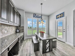 A kitchen with a granite countertop, wooden flooring, a bench, and a view of the outdoors through a window.
