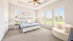 A bedroom with a bed, bedside tables, a nightstand, a curved seating area, and large windows.