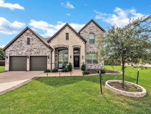 A two-story stone house with a garage, a front porch, and a well-maintained lawn.