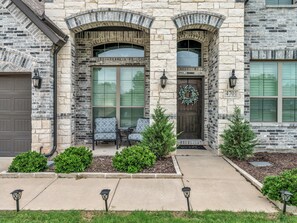A stone building with a garage, a front door with a wreath, and a small porch with chairs.