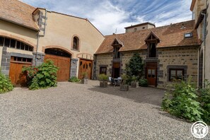 A courtyard with stone buildings, wooden doors, and a gravel ground. - The Gates of Baudet (MIREFLEURS)