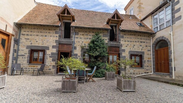 Ein Steinhaus mit Innenhof, Holzläden und einem kleinen Tisch mit Stühlen.
