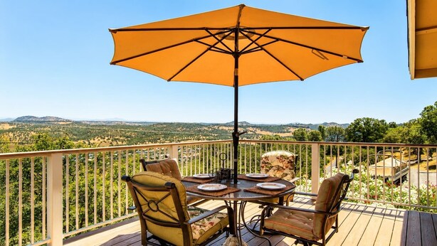 Una terraza con mesa y sillas, un paraguas y vistas a viñedos.