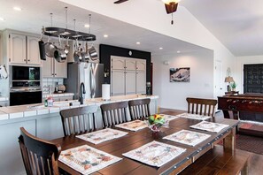 Une cuisine moderne avec un coin repas, comprenant un grand îlot central, des ustensiles de cuisine suspendus et une horloge au mur.