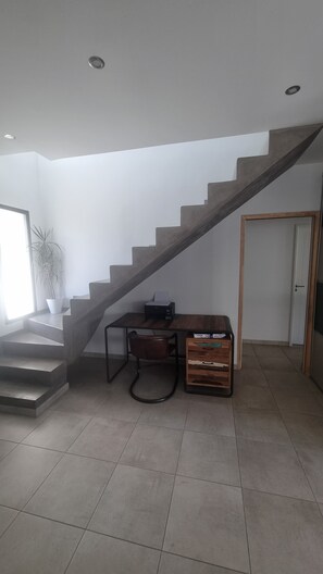 Una escalera que lleva al segundo piso, un escritorio con una impresora, una planta en maceta y una puerta.