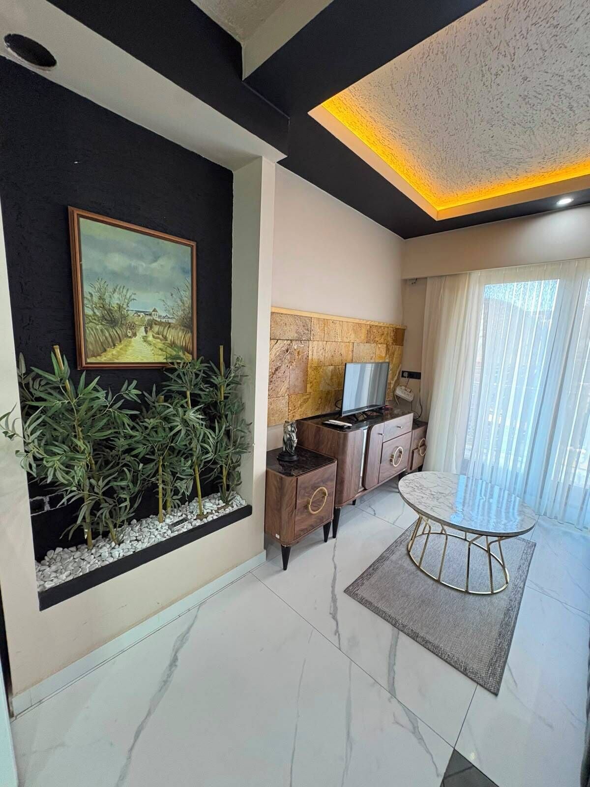 A modern living room with a painting, plants, a TV, and a dining area.