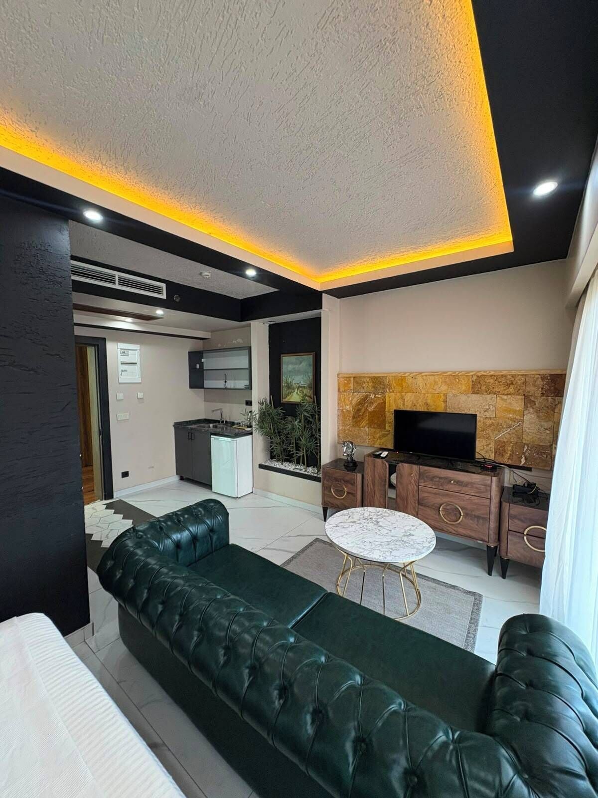 A modern living room with a green sofa, a marble coffee table, and a kitchen area with a TV.