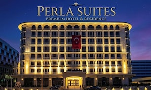 A multi-story hotel with a prominent entrance, a flag, and a well-lit facade. - PERLA SUİTES (İstanbul)