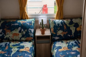 A cozy interior with two beds featuring animal-themed bedding, a small table with a potted plant, and a window with curtains.