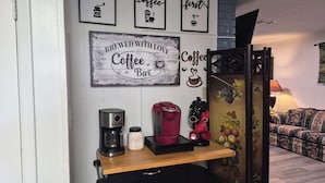 A coffee station with a coffee maker, a milk frother, and a mug on a wooden shelf.