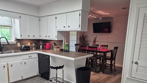 A modern kitchen with white cabinets, a dining area with a red table, and a TV mounted on the wall.