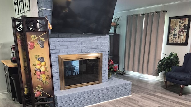 A living room with a fireplace, a flat-screen TV mounted above it, a wooden coffee table, and a floral sofa.