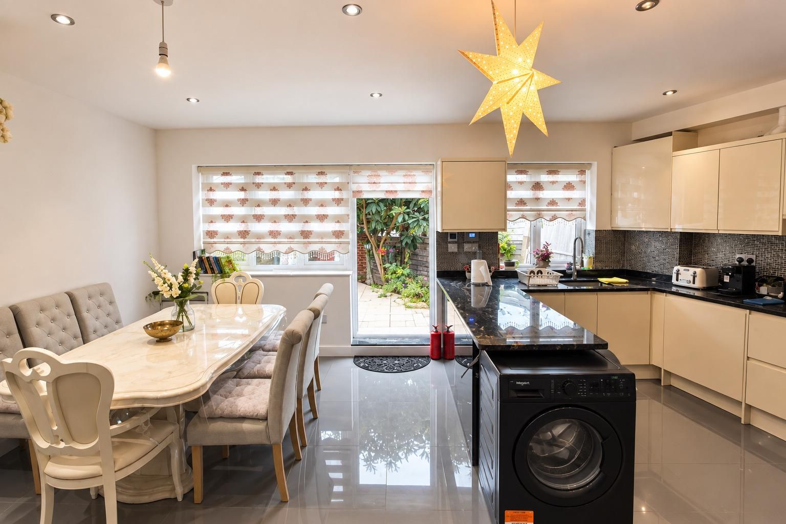 A modern kitchen with a built-in washer, a dining area with a table and chairs, and a large window with blinds.