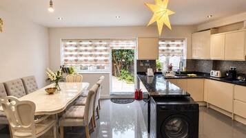 A modern kitchen with a built-in washer, a dining area with a table and chairs, and a large window with blinds.