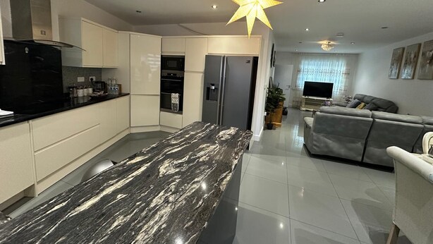 A modern kitchen with a marble countertop, a built-in oven, and a dining area with a grey sofa. - Greenview Manor house in Tottenham North London 4BRM 2bath (London)