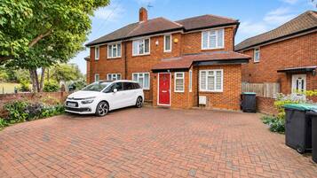 A two-story brick house with a red door, a white car parked in the driveway, and a brick pathway leading to the entrance.