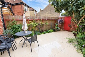 A patio with a round table and chairs, surrounded by a brick wall and a wooden fence. - Greenview Manor house in Tottenham North London 4BRM 2bath (London)