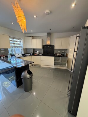 Een moderne keuken met een centraal eiland, witte kasten, een zwarte koelkast en een decoratieve lamp.