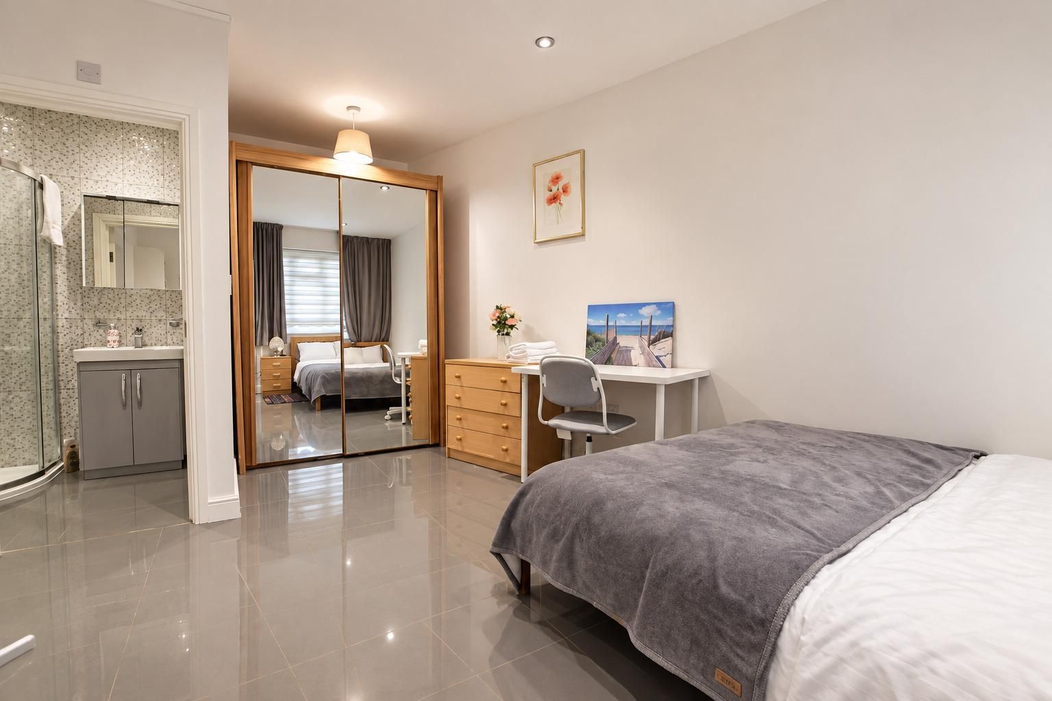 A modern bedroom with a bed, a desk, a chair, a wardrobe, and a bathroom with a shower and a mirror.