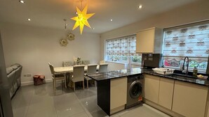 A modern kitchen with a star-shaped light fixture, a dining area with a table and chairs, and a washing machine. - Greenview Manor house in Tottenham North London 4BRM 2bath (London)