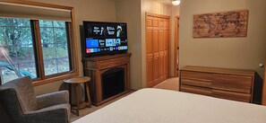 A bedroom with a television, a fireplace, a wooden dresser, a chair, and a map on the wall.