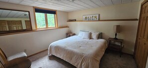 Een slaapkamer met een bed, nachtkastje, lamp, raam, spiegel en een schilderij aan de muur.