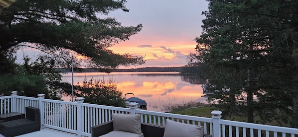 A deck with outdoor furniture overlooking a calm lake at sunset.