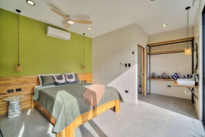 A modern bedroom with a bed, a ceiling fan, an air conditioner, and a bathroom with a towel rack. - Villas Tsuru (Hone Creek)