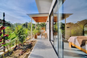A modern house with a glass-enclosed patio, a wooden deck, and a bed with a blanket. - Villas Tsuru (Hone Creek)