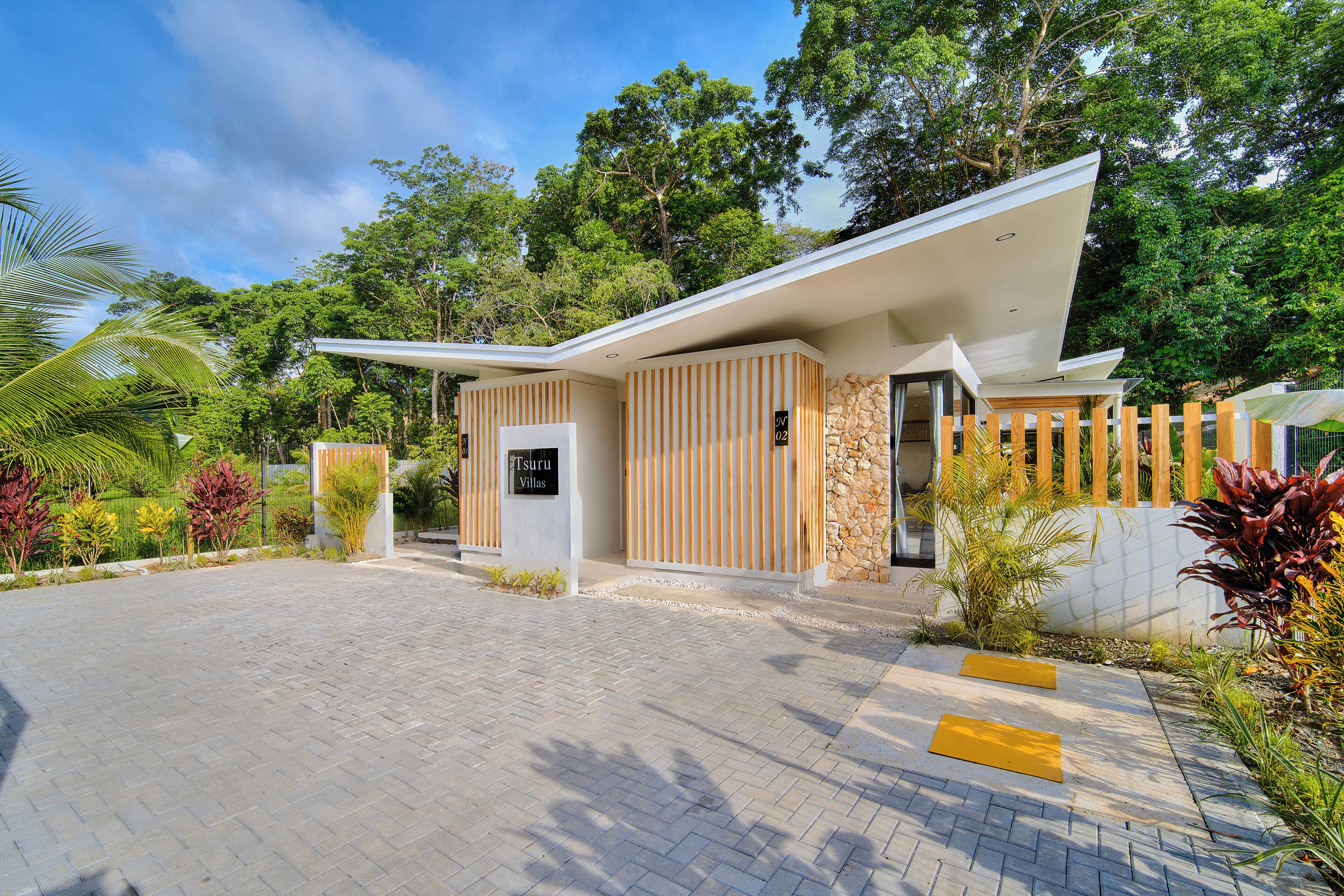 A modern villa with a paved driveway, a wooden fence, and a stone wall.