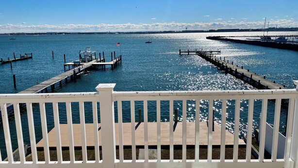 A waterfront view from a wooden deck with a white railing, a dock extending into the water, and a clear blue sky. - Big Waterfront House! Fishing Dock, Arcade, Garage Parking, Walk to Beach! (Norfolk)