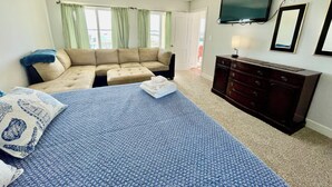 A bedroom with a bed, a sofa, a dresser, a television, and a window with curtains. - Big Waterfront House! Fishing Dock, Arcade, Garage Parking, Walk to Beach! (Norfolk)